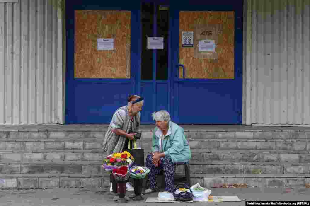 Женщины продают цветы и овощи возле закрытого супермаркета. В городе не работают крупные супермаркеты и торговые центры. Открыты лишь небольшие продуктовые магазины